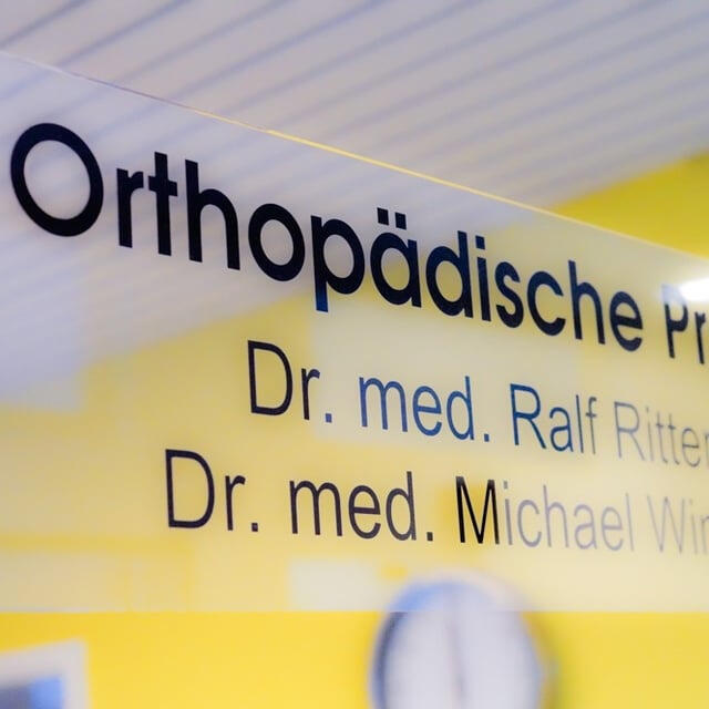 Eingangsbereich der orthopädischen Praxis mit Praxisschild und den Namen der behandelnden Ärzte.